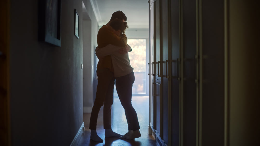A grieving couple hugging in a hallway