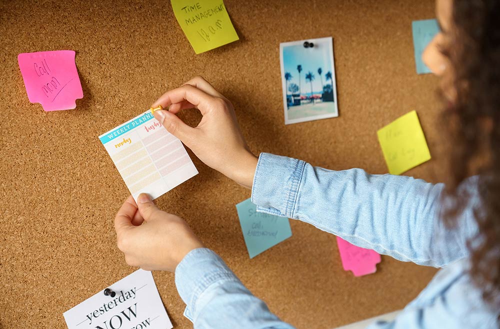 A person posting a planner to a corkboard