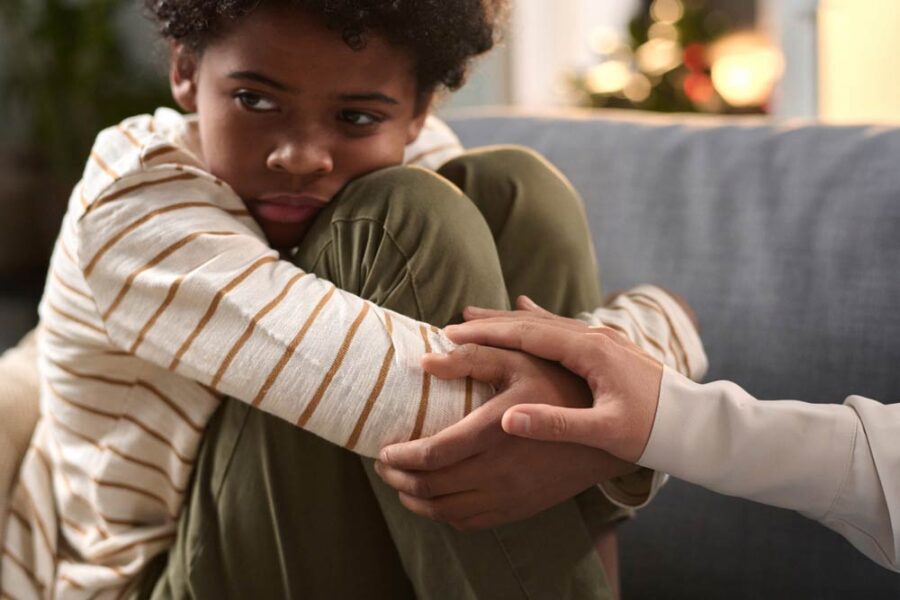 A sad child hugging his knees and being comforted