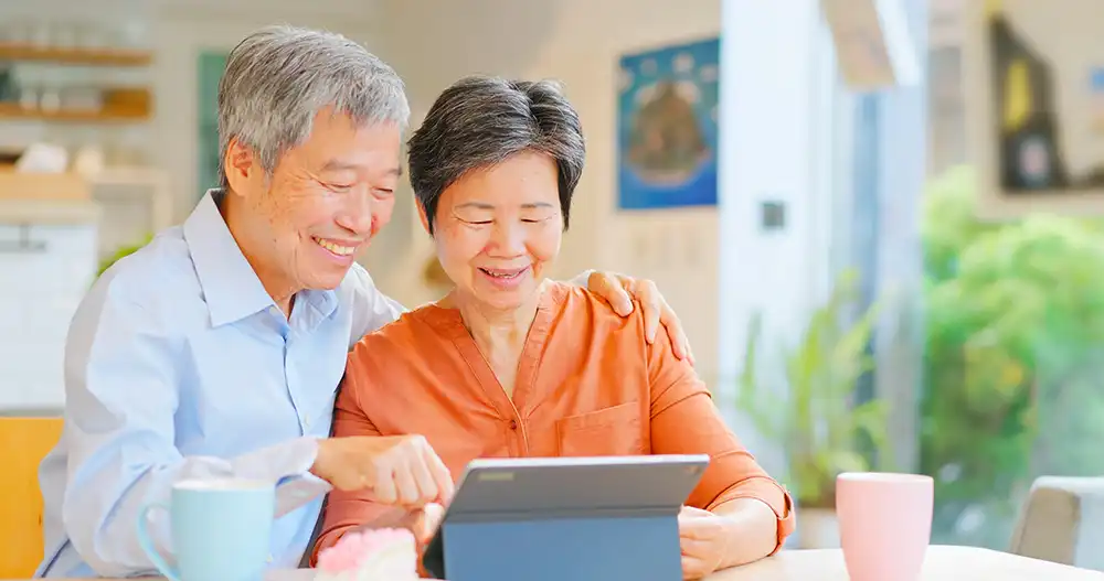 An elderly couple smiling while using a tablet
