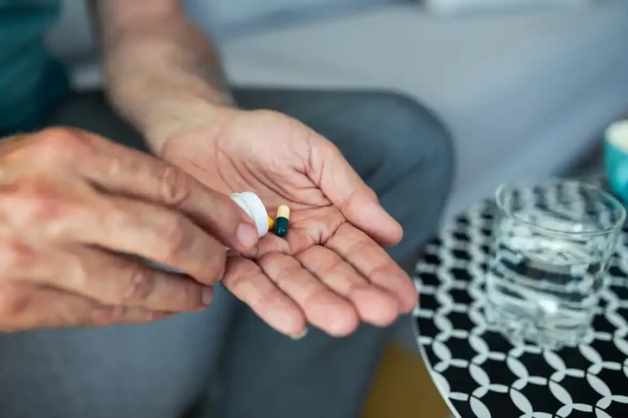 Hands of an elderly man taking a pill with water.